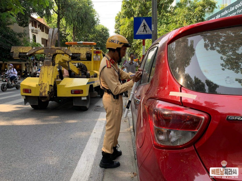 자동차 주차위반으로 노랑색 교통경찰이 차량의 문에 스티커를 붙이고 차량압수를 위해 서류를 작성하고 있다 (이미지 출처: internet)